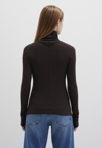 Brown long-sleeve top with a high collar, fitted shape, and smooth texture, paired with light blue, loose-fitting denim jeans featuring back pockets.