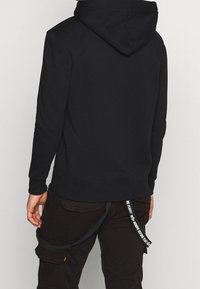 Felpa nera con cappuccio, dotata di orlo e polsini a coste, realizzata in materiale morbido. Presenta un cappio con motivo e una vestibilità comoda.