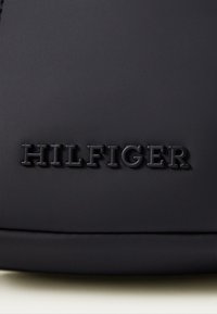 Svart material med en slät yta som har ett präglat "HILFIGER"-logotyp. Designen är minimalistisk utan synlig hårdvara eller accenter.