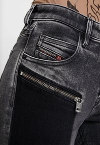 Černé a šedé džíny vyrobené z denimu, které mají kapsu na zip, kontrastní tkaninové panely a texturovaný povrch s jemným brandingem na pase.