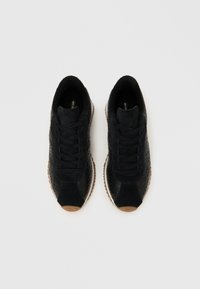 Μαύρα αθλητικά παπούτσια με υφασμένο δερμάτινο επάνω μέρος, σουέτ λεπτομέρειες και μαύρα κορδόνια, με καφέ λαστιχένια σόλα και λευκή μεσαία σόλα.