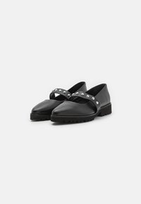 Zapatos de cuero negro con un diseño de punta afilada, que cuentan con una amplia correa con tachuelas a lo largo del empeine y una suela texturada y resistente.