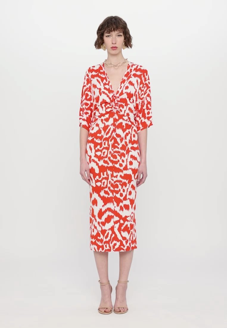 Robe à motifs rouges et blancs avec un décolleté en V profond, des manches courtes et un détail de nœud à l'avant, tombant jusqu'au mi-mollet. Texture de tissu lisse.
