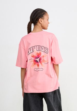 Tricou roz supradimensionat din bumbac, cu un grafic floral colorat pe spate și cu logo-ul "Adidas" într-un font îndrăzneț.