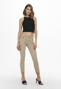Beige cargo pants with ribbed black crop top. Pants feature side pockets and gathered ankles. Model wears black heeled sandals.