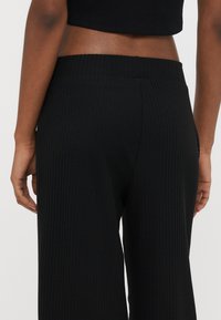Črne rebraste palazzo hlače z oprijetim pasom, ki imajo teksturirano površino in široke nogavice, ki se proti gležnju zožujejo.