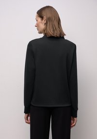 Felpa nera con collo alto e maniche lunghe. Tessuto liscio, vestibilità rilassata e polsini a coste. Design minimalista, senza motivi visibili.