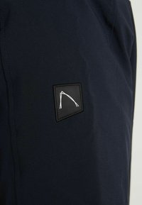 Granatowa tkanina z naszywką przedstawiającą biały geometryczny wzór przyszyty na teksturowanej powierzchni, prezentujący elegancki i nowoczesny design.