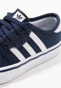 Mörkblå canvas sneakers med vit gummisula, med tre vita ränder, runda snören och en svartvit logotagg på tungan.