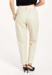 Beige faux leather trousers with a tapered design, high waist, and two back pockets, paired with black heel sandals.