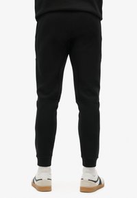 Zwarte taps toelopende sweatpants met ribbelmanchetten en zijzakken, gemaakt van zacht materiaal, gecombineerd met beige sneakers en witte sokken.