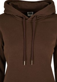 Sudadera con capucha marrón con cordón que presenta puntas de metal. La tela es suave con un acabado ligeramente texturizado. Etiqueta de Urban Classics visible.