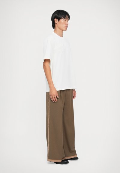 T-shirt bianco a maniche corte abbinato a pantaloni larghi marroni con una striscia laterale. Design minimalista con una vestibilità rilassata e tessuto morbido.