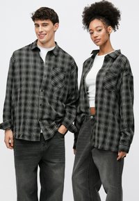 Črno-bele karirane srajce z dolgimi rokavi, z gumbi spredaj in prsni žepi, kombinirane z sivimi širokimi kavbojkami. Gladek tekstura tkanine.