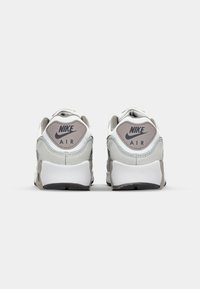 Nike Air kedas pelēkā un baltā krāsā. Iespējas ietver mīkstu apkakli, teksturētu sieta augšdaļu un firmas logotipu uz papēža. Teksturēta gumijas zole.