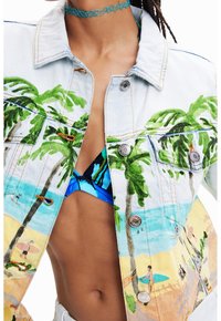 Jeansjacka med färgglad strand- och palmskrivning bärs över en blåmönstrad bikiniöverdel och en turkos chokerhalsband.
