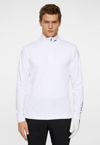 Valkoinen pitkähihainen neule, jossa on puolivetoketju, valmistettu teksturoituneesta kankaasta. Sisältää hillityn logon kauluksessa ja brändäyksen hihassa.