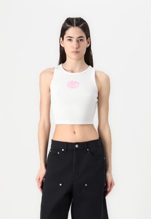 Top cropped branco com textura canelada, apresentando um logo rosa "Obey" centrado no peito. Combinado com calças pretas de cintura alta.
