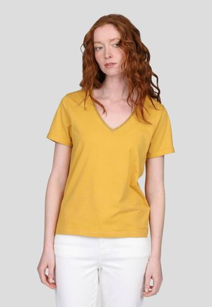 T-shirt jaune à col en V avec manches courtes, présentant un col texturé. Associé à un pantalon blanc en tissu lisse, au design décontracté.
