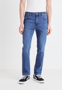 Niebieskie dżinsy z prostym krojem nogawki, pięcioma kieszeniami i kontrastowym przeszyciem, w połączeniu z czarno-białymi trampkami.