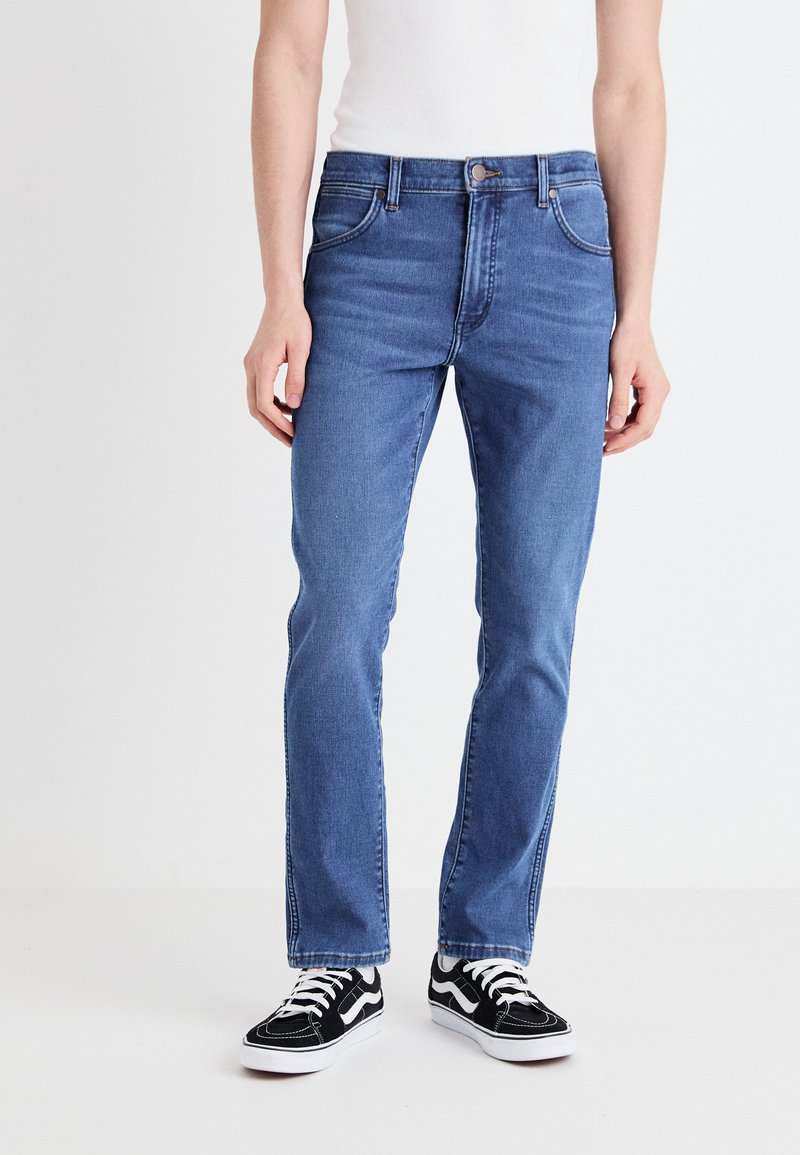 Niebieskie dżinsy z prostym krojem nogawki, pięcioma kieszeniami i kontrastowym przeszyciem, w połączeniu z czarno-białymi trampkami.