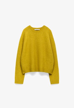 Gul stickad tröja med rundad halsringning, avslappnade axlar och ribbade ärmslut. Mjuk textur, cropped design och minimal logotyp.