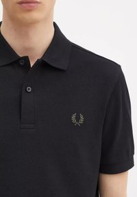Polo shirt nera realizzata in tessuto testurizzato, con scollatura a due bottoni e logo ricamato verde oliva sul lato sinistro del petto.