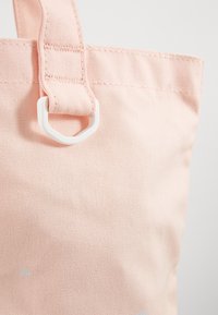 Różowa torba na ramię z płótna o teksturowanym wykończeniu i materiałowym uchwytem. Posiada biały plastikowy akcent przy mocowaniu uchwytu.