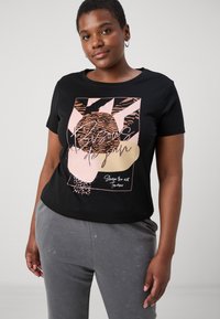 Black short-sleeve t-shirt featuring a colorful geometric print, including animal patterns and text, paired with gray textured pants.