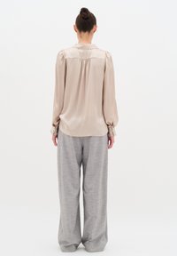 Blusa beige, setosa, a maniche lunghe con una piega sul retro, abbinata a pantaloni larghi grigio chiaro realizzati in un tessuto testurizzato.