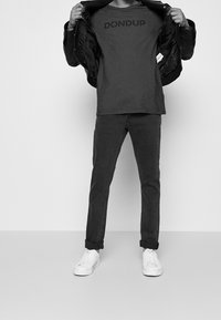 Camiseta gris con el logo "DONDUP", combinada bajo una chaqueta negra, acompañada de jeans oscuros y zapatillas blancas. Textura suave, estilo casual.