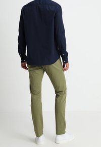 Laivastonsininen pitkähihaisen paita, kapealla leikkauksella ja napilliset kalvosimet. Yhdistetty oliivinvihreisiin chinoshousuihin ja valkoisiin lenkkareihin, luoden rento ilmeen.