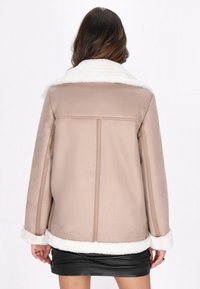 Jachetă din faux suede bej cu guler și mansete din blană sintetică albă, având o croială lejeră, dreptă și detalii de cusătură contrastante.