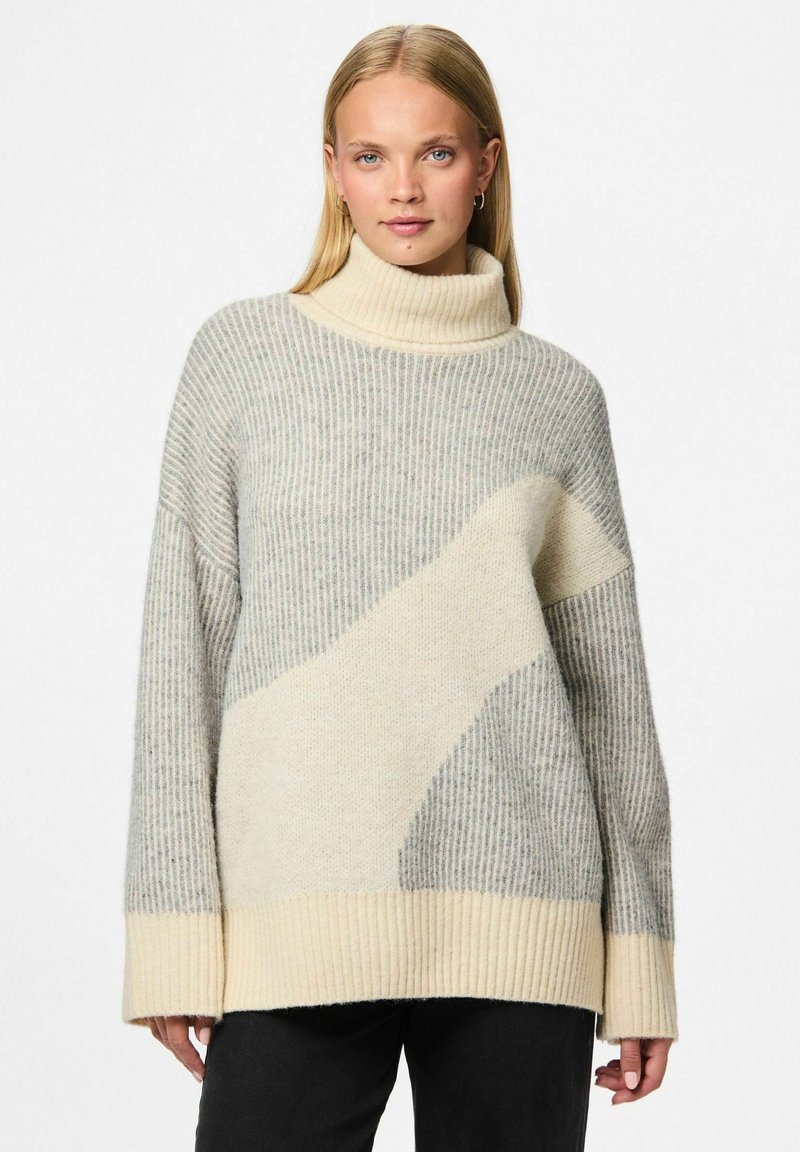 Heledhalli ja kreemjas kampsun kõrge kaelusega ja soonikuid imiteeriva tekstuuriga, millel on ees suur kreemjas abstraktne muster ja pikad varrukad.