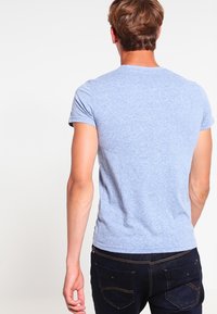 Lichtblauw T-shirt met korte mouwen van zachte stof, met een ronde halslijn en een nauwsluitend ontwerp. Gecombineerd met donkere jeans.