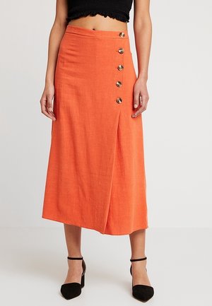 Jupe midi en lin orange avec des boutons sur le devant, un design portefeuille et une fente sur le côté, associée à des talons noirs.
