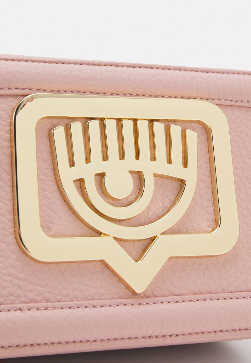 Borsa in pelle rosa con logo a occhio dorato su una struttura rettangolare. Presenta una superficie testurizzata e cuciture a contrasto lungo i bordi.