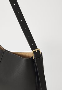 Black leather handbag with a smooth texture, featuring a flat strap with multiple holes and a gold-tone metal buckle as a detail.