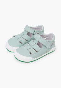 Sandalias de cuero verde con suelas de goma blanca, que cuentan con recortes abiertos y correas de velcro ajustables para poner y quitar fácilmente.
