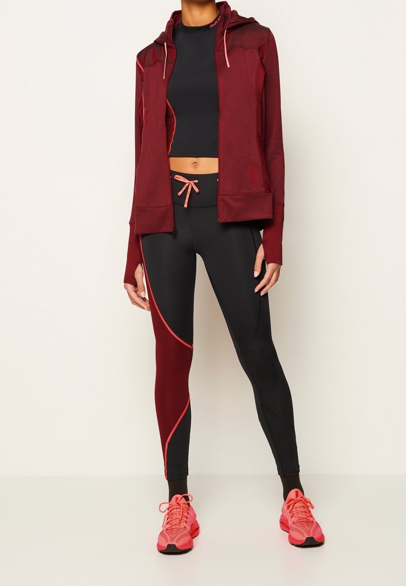 Kvinnors träningskläder: vinröd hoodie med rosa detaljer, svarta leggings med röda inslag och rosa löparskor. Har en kortad design.