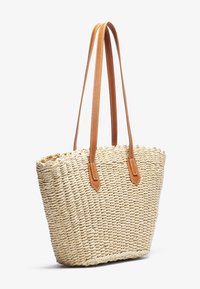 Sac cabas en paille tissée avec des anses en cuir marron clair, forme rectangulaire et surface texturée. Le bord supérieur présente un design effiloché pour plus de détails.