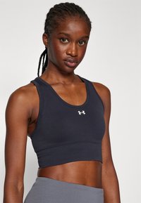 Sujetador deportivo negro tipo crop con diseño de espalda nadadora, fabricado en tejido elástico, presenta un pequeño logo blanco en la parte frontal y una textura acanalada a lo largo de la banda.