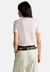 Světle růžové tričko s krátkým rukávem a kulatým výstřihem, spárované se krémovými kalhotami a černým páskem. Hladká textura, jednoduchý design a bez vzorů.