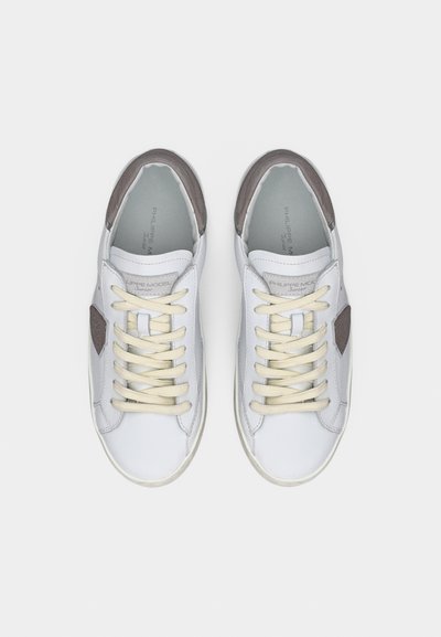 Baskets basses blanches avec des lacets beiges et des accents gris, vues de dessus sur un fond blanc uni.