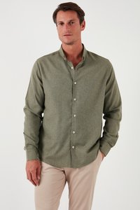 Camisa de manga larga en verde oliva, con botones y fabricada en una tela texturada, que presenta un cuello clásico y botones blancos. La lleva puesta con unos pantalones beige.