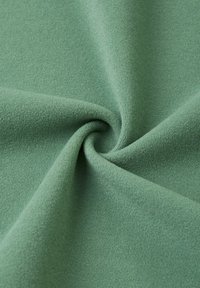 Tessuto morbido e testurizzato in verde salvia, con una superficie liscia e una leggera lucentezza, disposto a spirale per evidenziarne la flessibilità e la caduta.