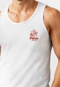 Weißes ärmelloses Tanktop mit einem roten Grafikdruck eines lächelnden Kochs mit einem Teller, beschriftet "Pälzer Deller." Glatter Stoff, entspannte Passform.