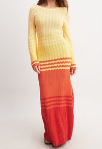 Robe maxi en maille à manches longues, présentant un dégradé de couleurs allant du jaune à l'orange puis au rouge, avec une texture ondulée et des rayures horizontales.