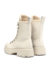 Białe skórzane botki z futrzanym wykończeniem, okrągłym noskiem, metalowymi oczkami i grubą gumową podeszwą. Sznurowadła mają dekoracyjne detale w postaci ozdobnych elementów.