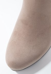 Gros plan sur la pointe d'une chaussure en daim beige avec une surface lisse et légèrement texturée sur un fond blanc.